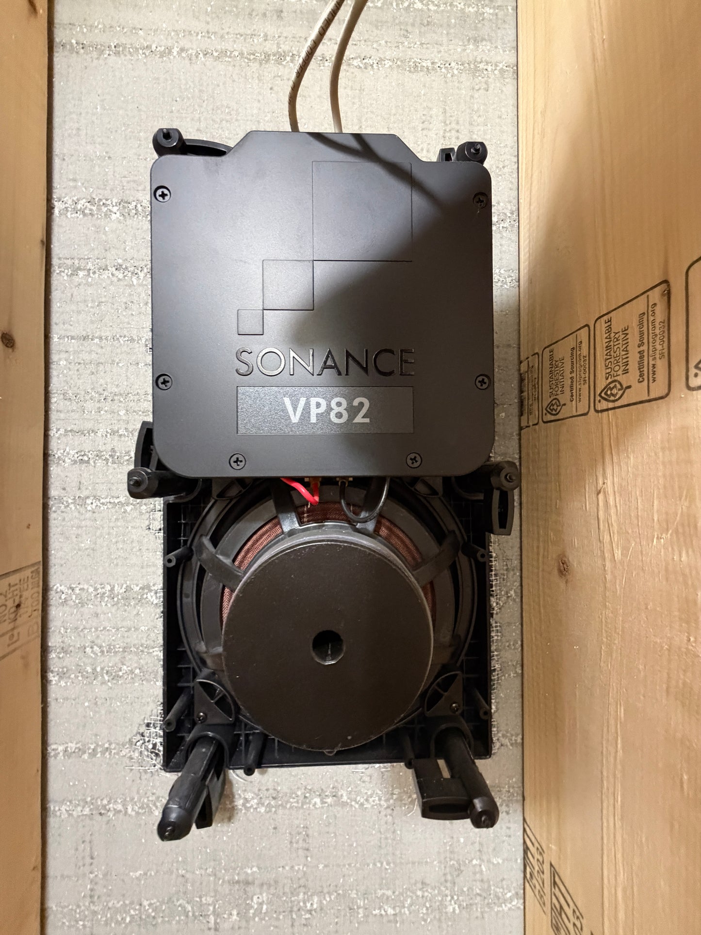 Sonance VP82 speaker on a wooden surface with a textured wall background