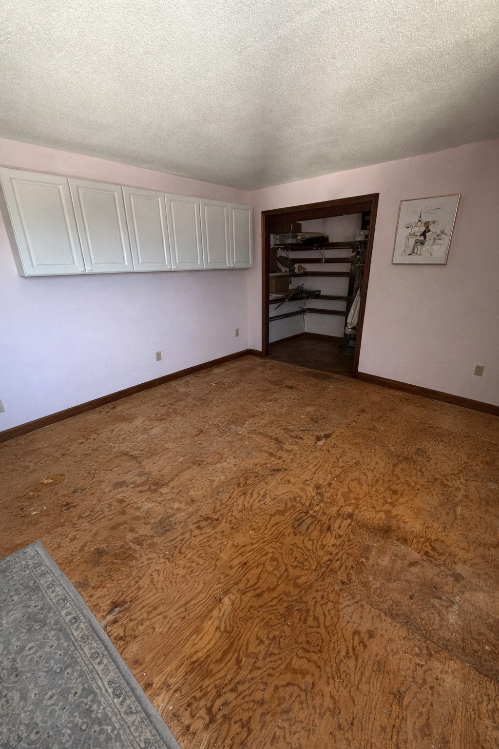 Empty room with wooden floor, white walls, and a door leading to another room.