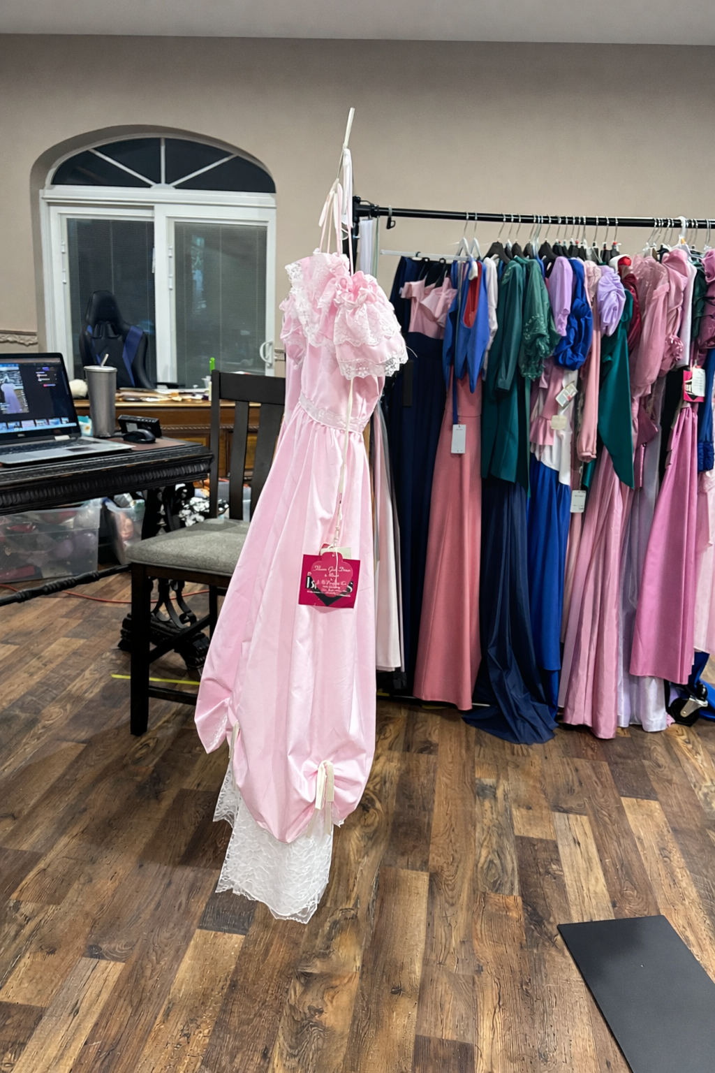 Pink dress hanging on a rack with other dresses in a room.