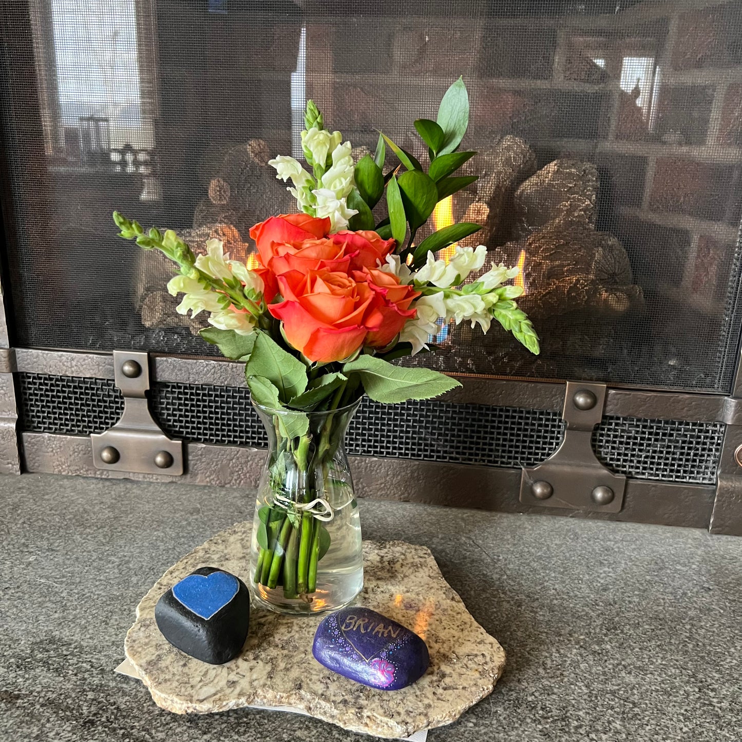 Bouquet of flowers in a vase on a stone coaster in front of a fireplace.