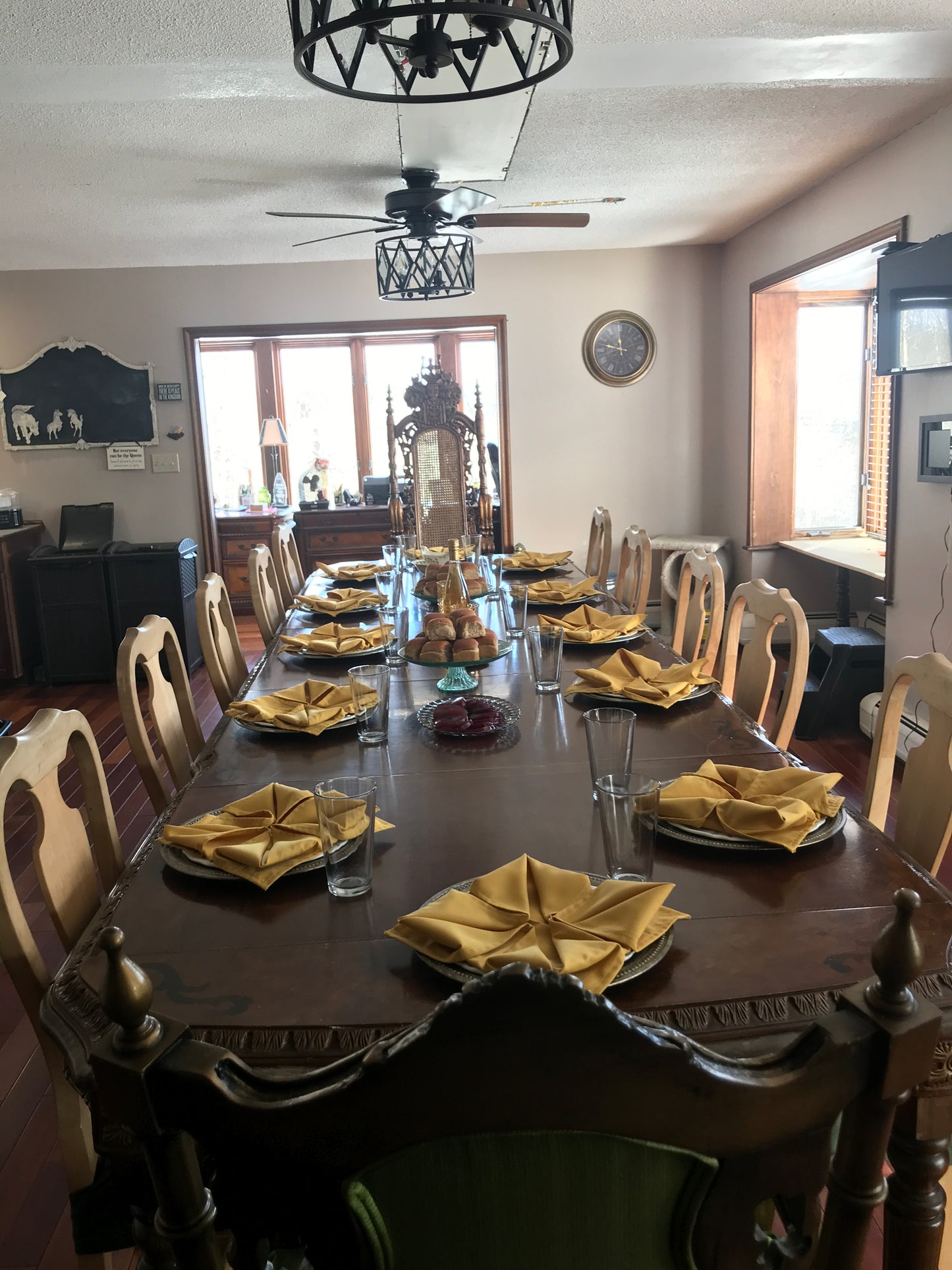 Dining room with a large wooden table set for a meal, featuring gold cutlery and folded napkins.