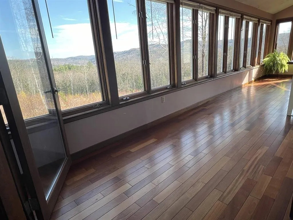 Large  sunroom with wooden floor and wall of windows overlooking a scenic landscape