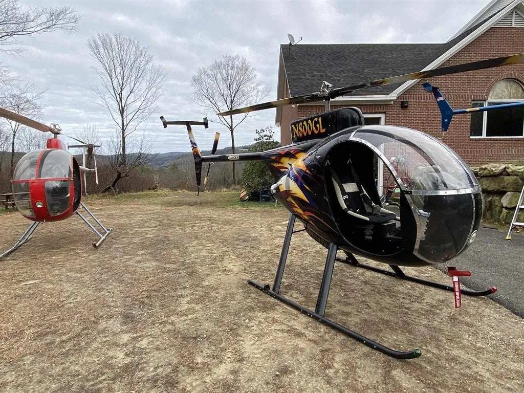 Two helicopters on a driveway looking across the back view  brick building in the background.
