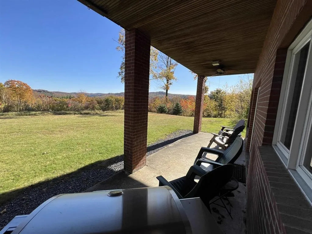 Covered outdoor patio area with chairs and a scenic view of trees  mountains and fields.