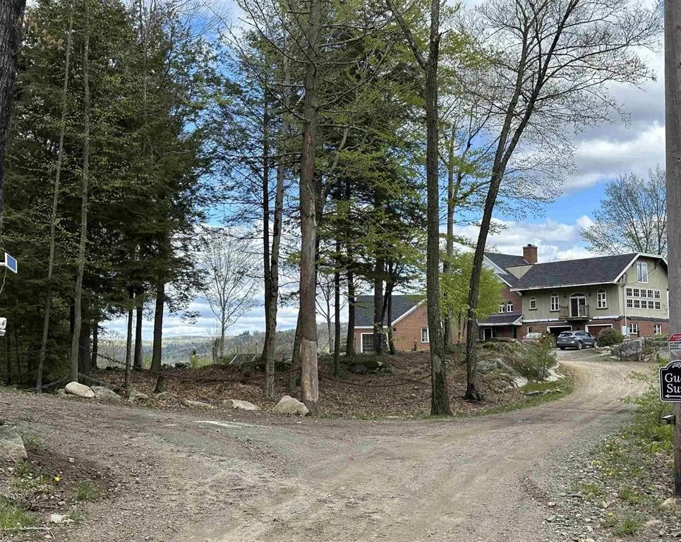 Circular driveway open views to a unique house surrounded by trees ledges and wildflowers.