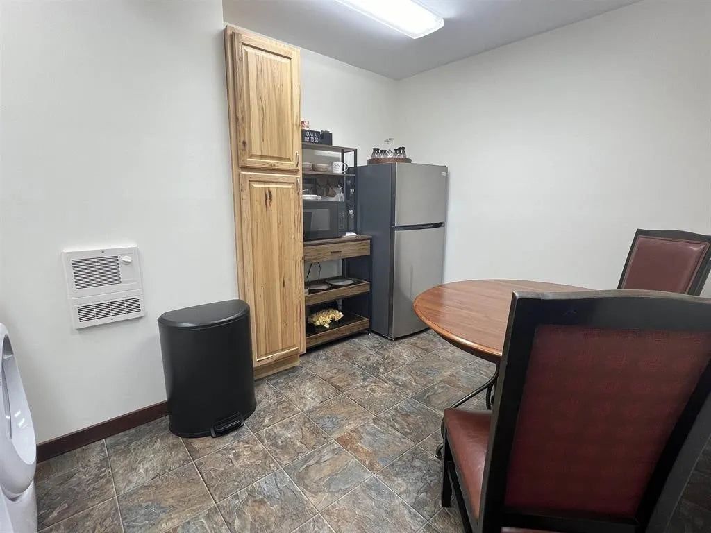 Small kitchenette with refrigerator, microwave, and table in a room with stone flooring.