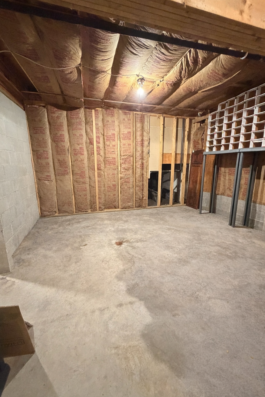 Wine room with unfinished walls and ceiling, concrete floor, and shelves.